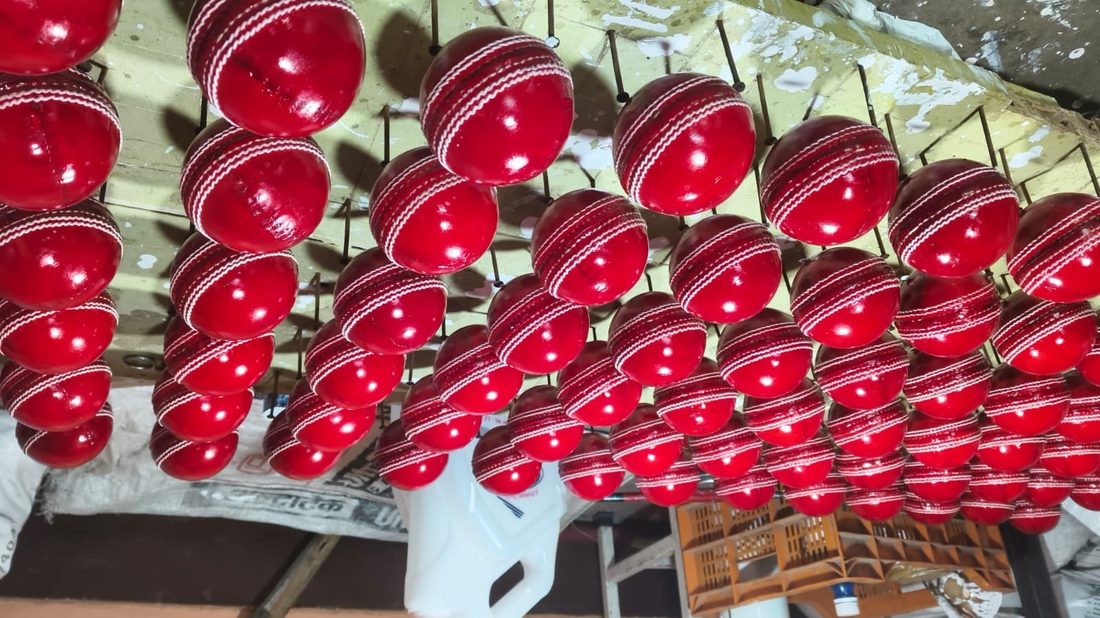 Hundreds of red leather cricket balls drying on pin racks in GEO SPORTS Meerut workshop after stitching