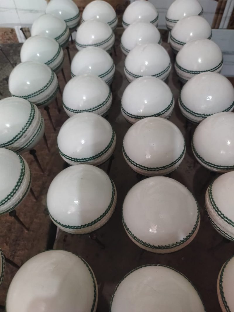 White cricket balls with green seam stitching, drying after production at GEO SPORTS workshop